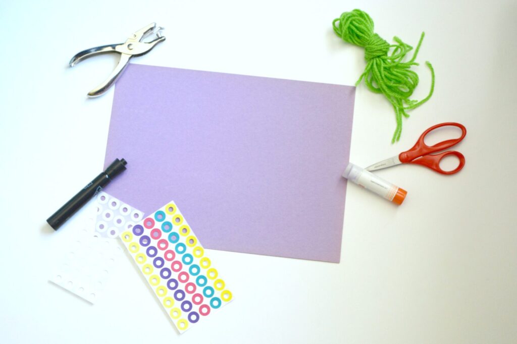 photo of items needed to make windsock octopus (hole punch, yarn, hole punch reinforcement stickers, scissors, glue stick, marker, colored construction paper)